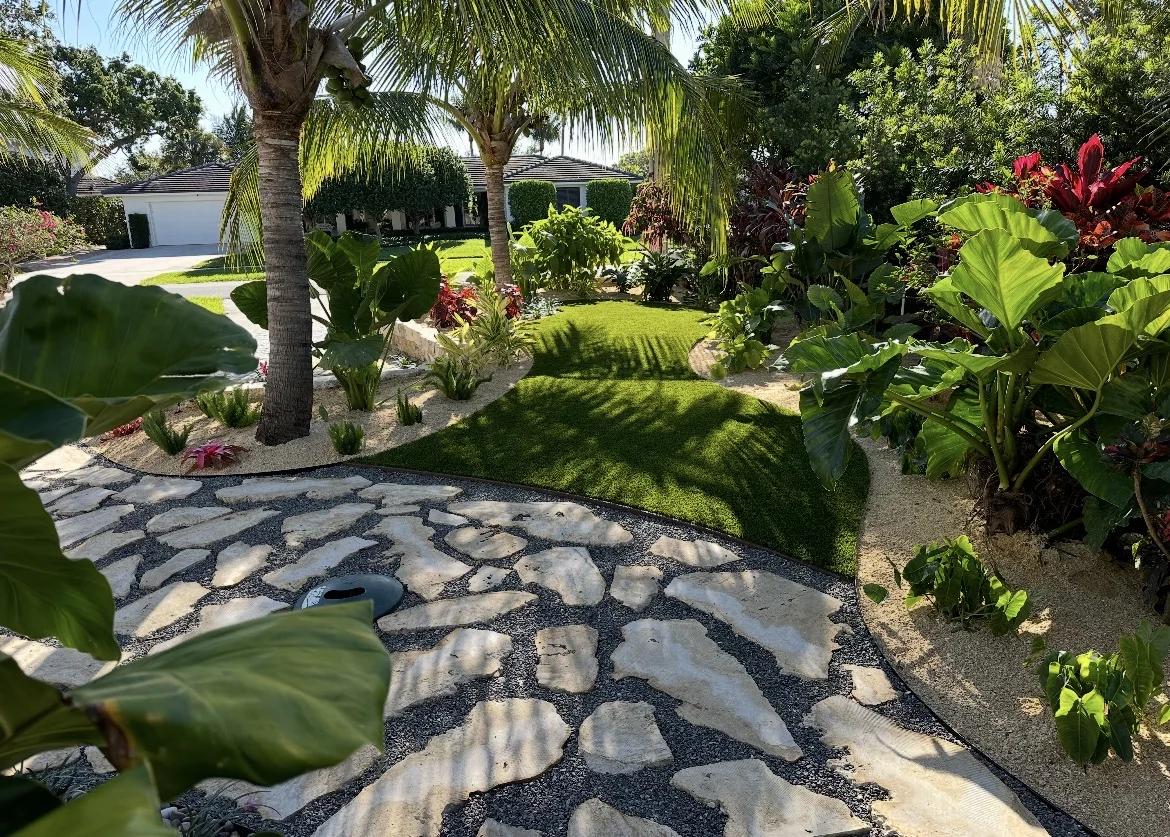 Tropical garden path with large flagstone pavers set in black pebble bordered by elephant-ear foliage