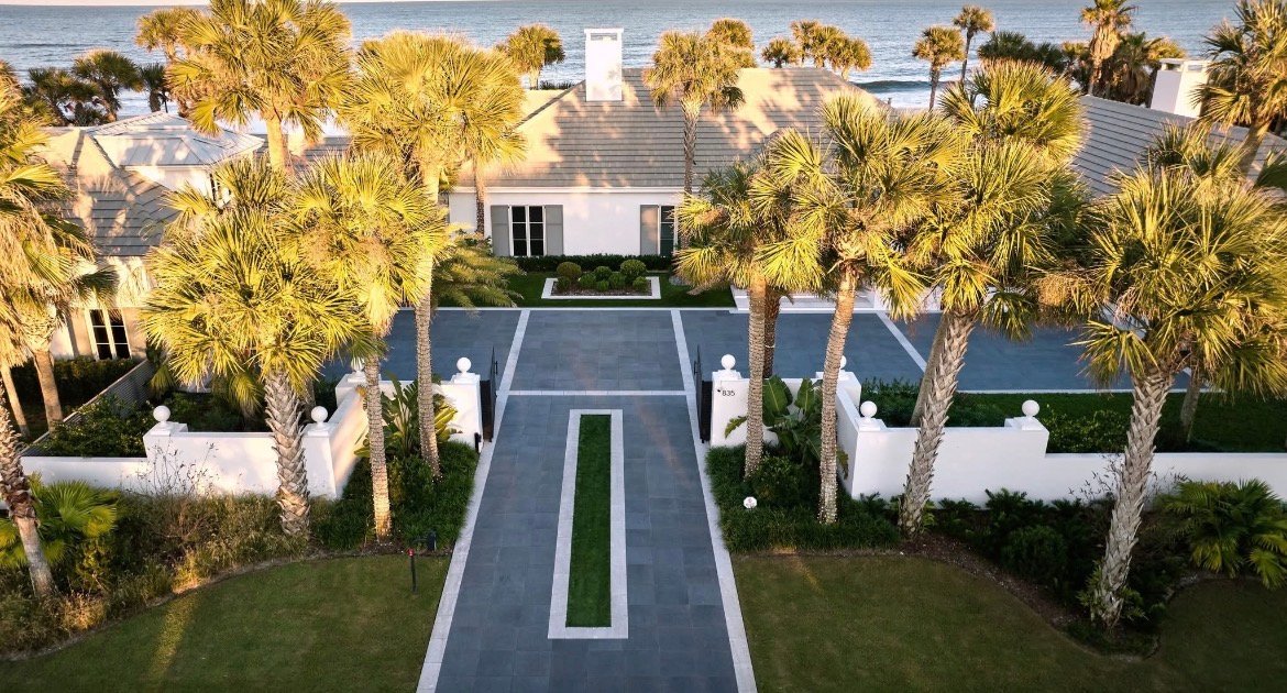 Beachfront estate with palm-lined paver driveway at golden hour