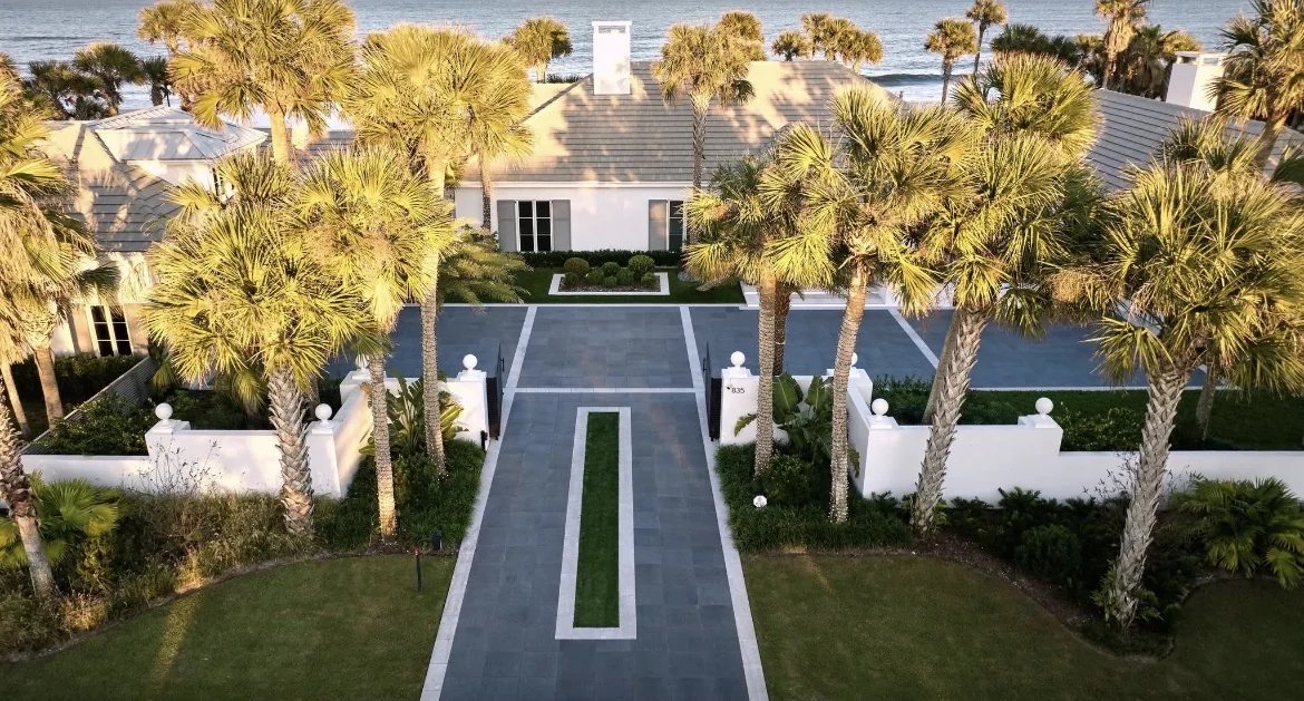 Aerial of a beachfront estate with a palm-lined paver entrance drive and formal landscape