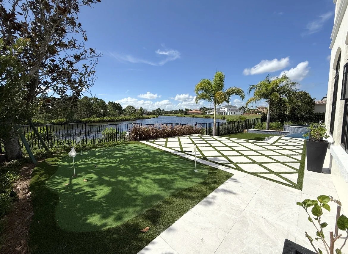 Backyard putting green with flags overlooking a lake, bordered by a bronze iron fence