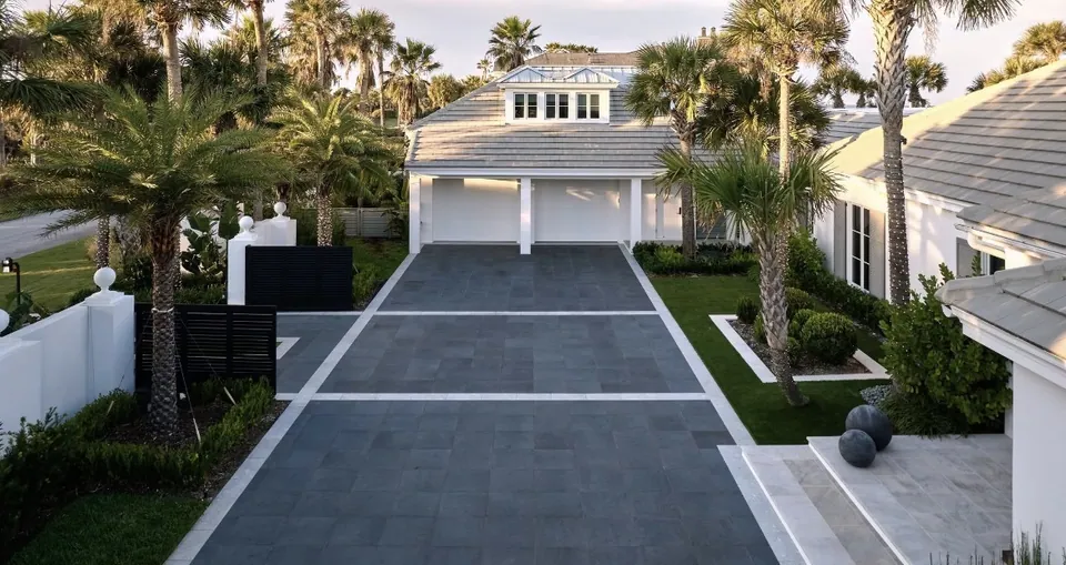 Aerial of a modern coastal home with a charcoal paver driveway and white travertine accent strips