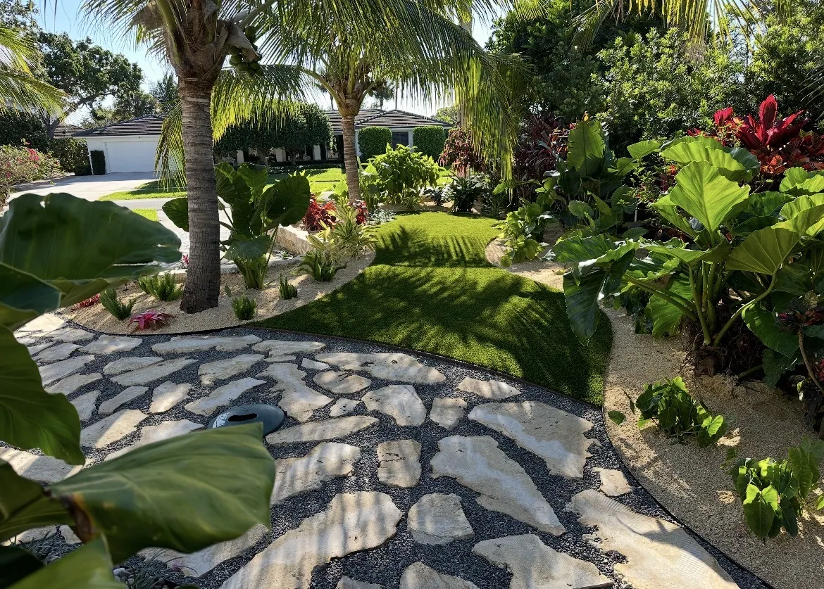 Tropical garden path with large flagstone pavers set in black pebble bordered by elephant-ear foliage